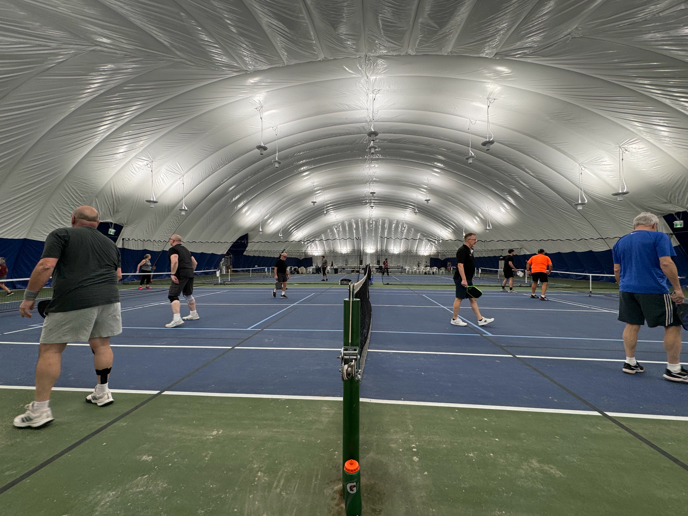 Indoor pickleball under a domed roof, several courts in play at once