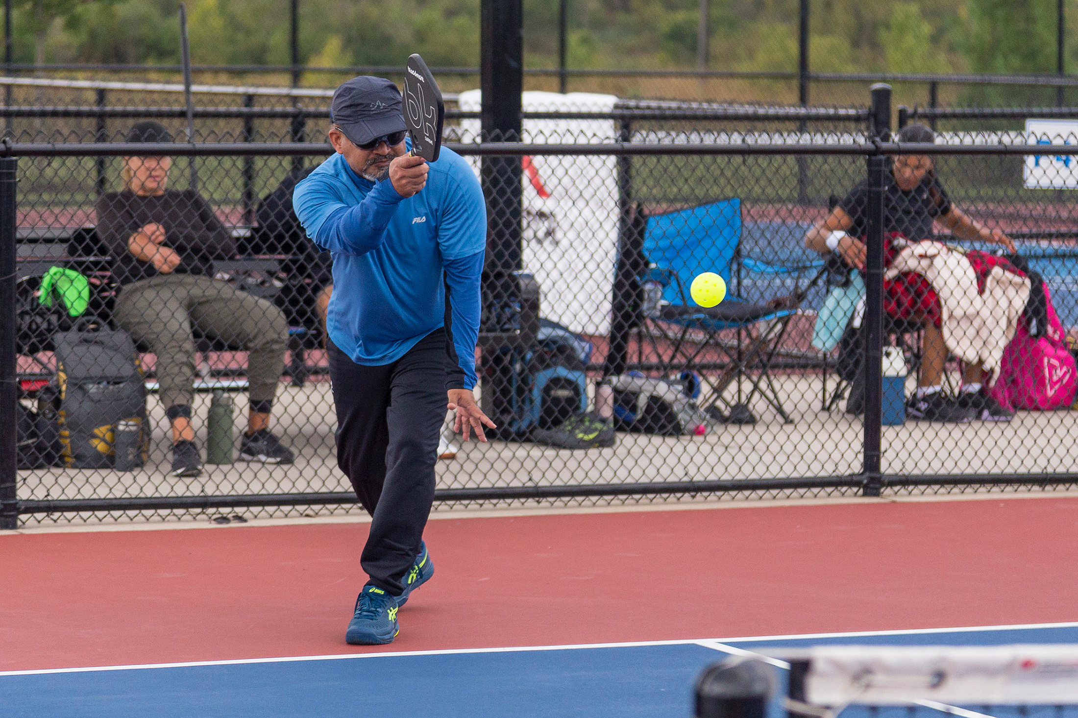 A player returning a shot on an outdoor Niagara court, others waiting courtside